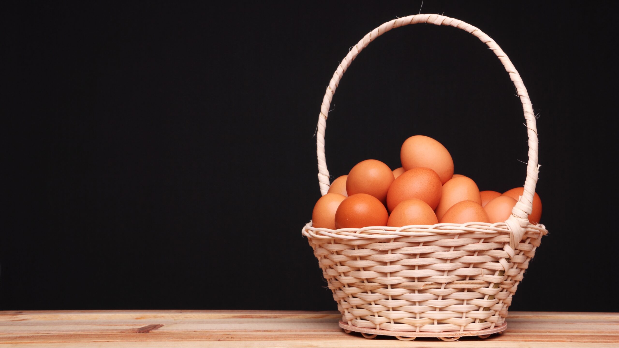 Black background with a basket, containing eggs. on a wooden table representing donor egg cost.