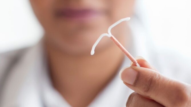 women's face faded in the background while she holds an IUD in one hand representing can you be an egg donor with an iud.