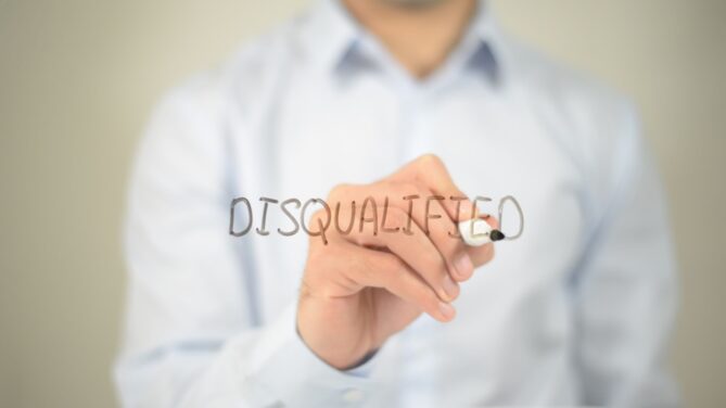 Man in a collared shirt writing the word "disqualified" on a mirror with black marker representing what disqualifies you from being a sperm donor.