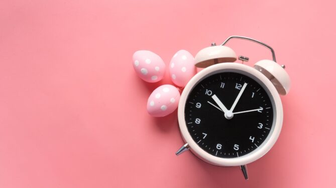 A clock that has pink eggs next to it laying on a pink background representing how many times can you donate eggs