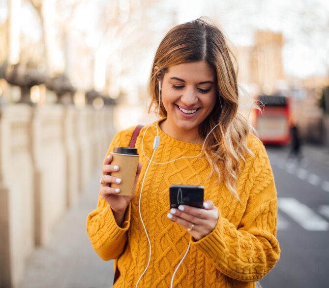 A woman in a bright yellow sweater looking down at her phone representing how to become an egg donor in Arizona.