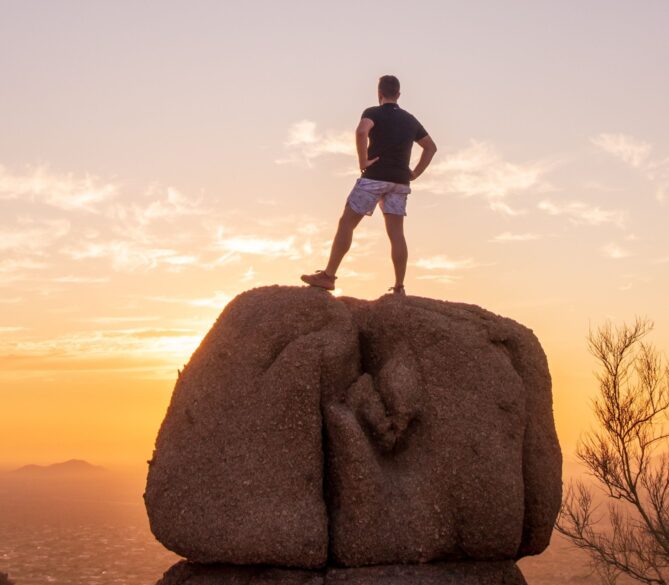 A man standing on a huge rock staring out into the distance as the sun sets representing sperm donor.