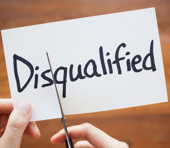 A hand cutting a paper that says disqualified representing egg donation disqualifiers.