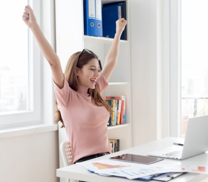 A women sitting at a desk with here arms up high in excitement representing how much do egg donors make.