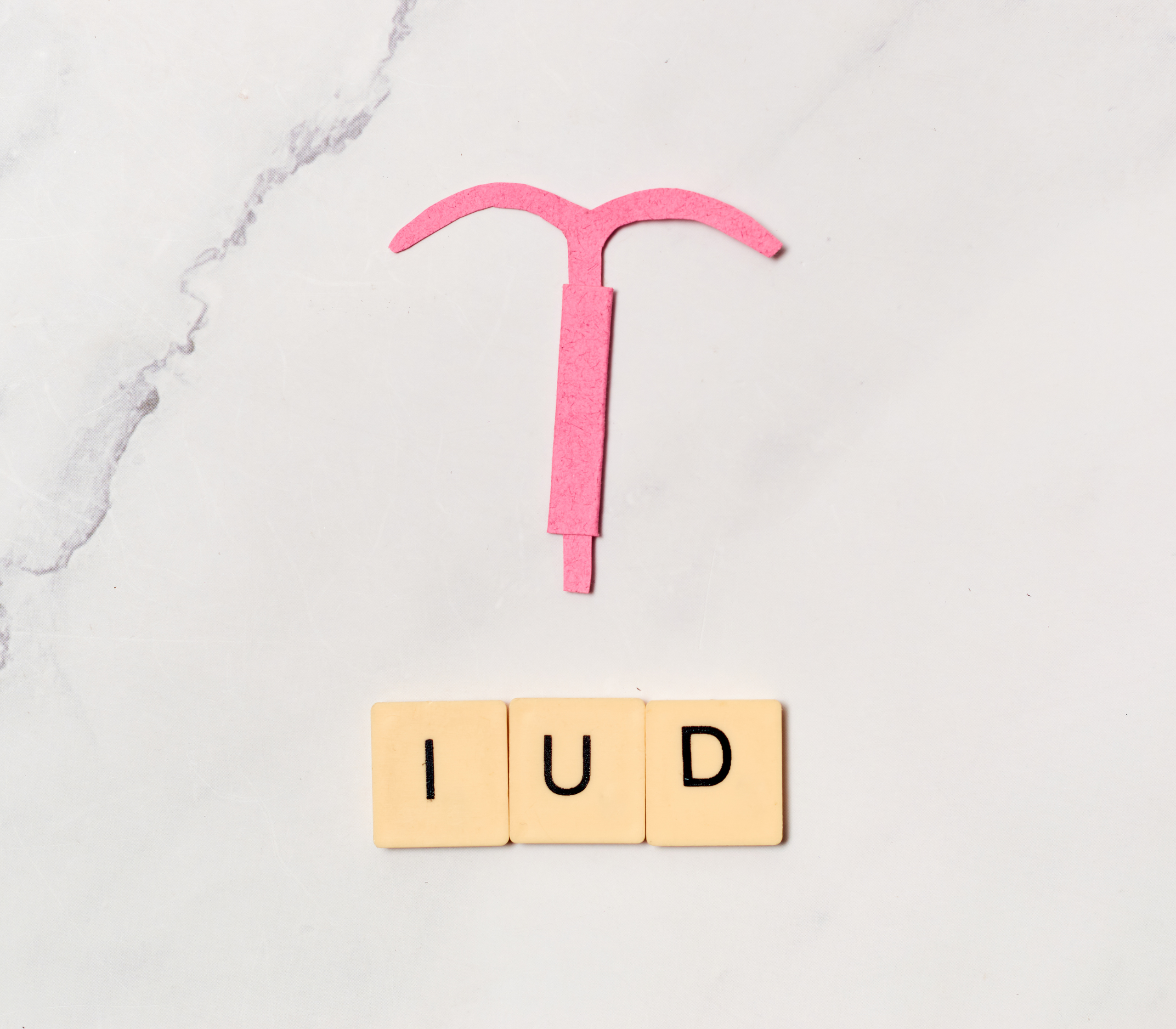 A pink IUD laying on a whit marbled surface.