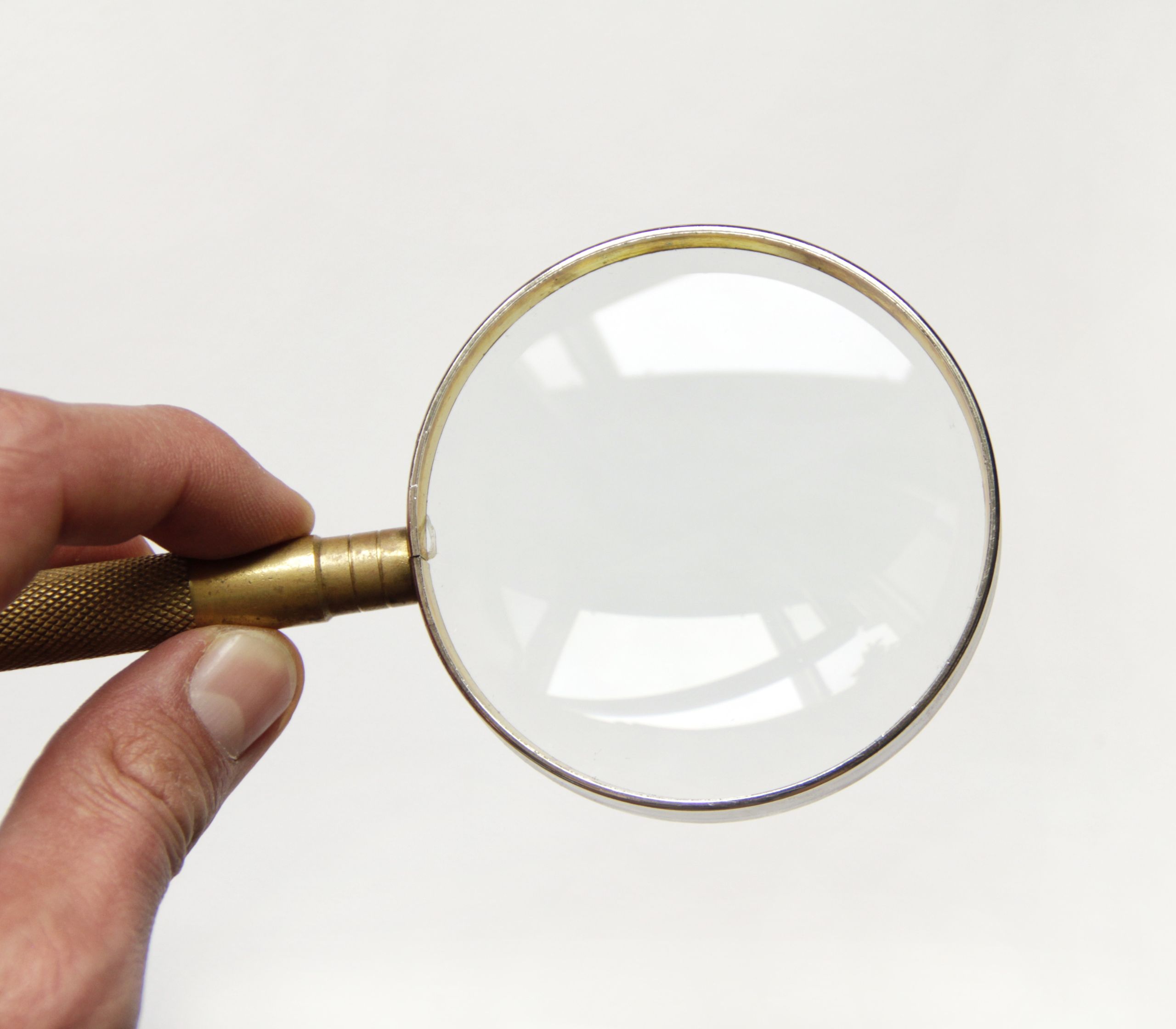 A close up of a white mans hand holding a magnifying glass to represent how to find an egg donor that looks like you